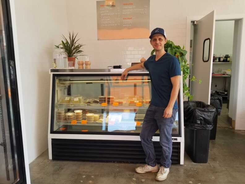 A man in a ball cap and T-shirt leans in front of a glass front display counter.