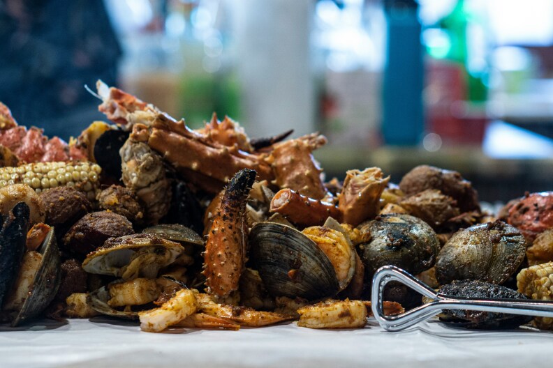 An assortment of cooked fish at a seafood establishment in Long Beach. Crab legs and other shelled fish is strewn on a platter, with roasted corn among the pile too.