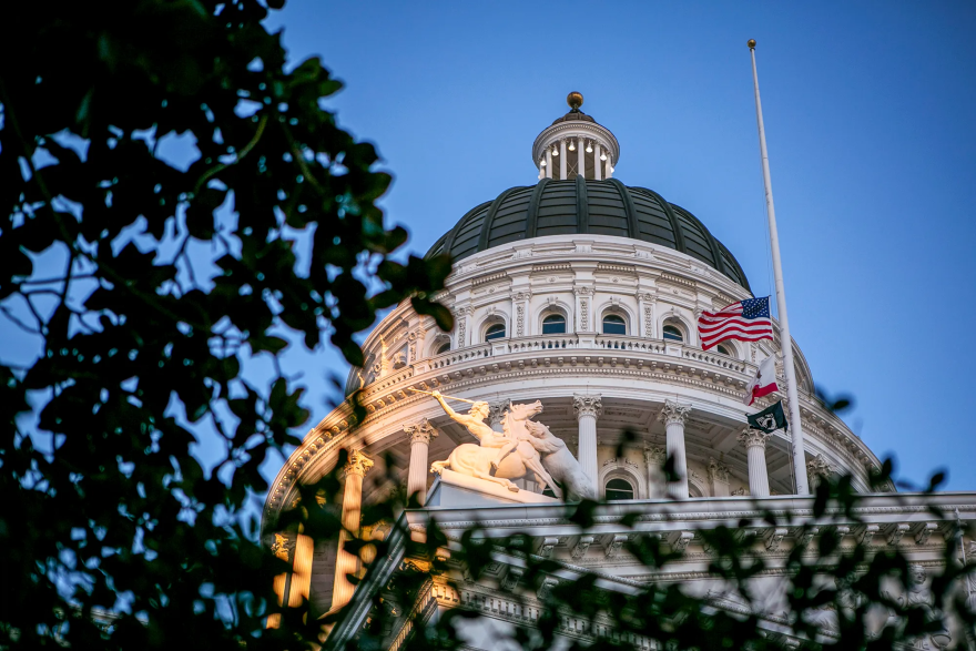 The California state capitol dome shown with flags waving on a pole next to it.