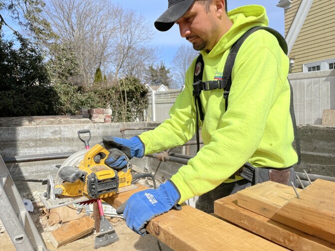 A man uses a circular saw on a board.