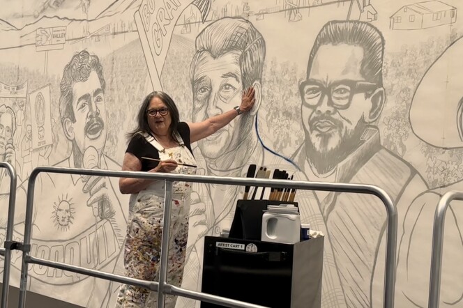 Judy Baca stands in front of the likeness of Cesar Chavez