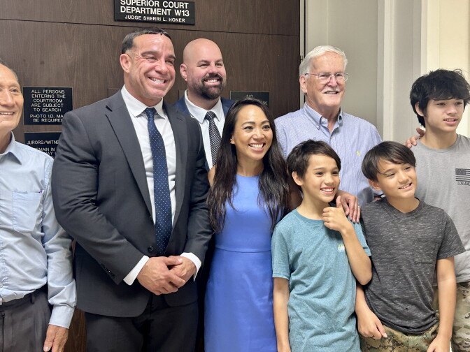 A group of adults and children smile together outside a courtroom door labeled Superior Court Department W13.