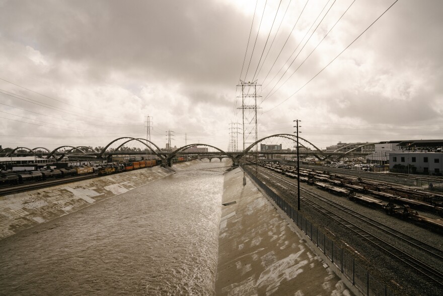 The L.A. River's water flows under an overcast sky, a mix of white and golden light illuminating the scene.