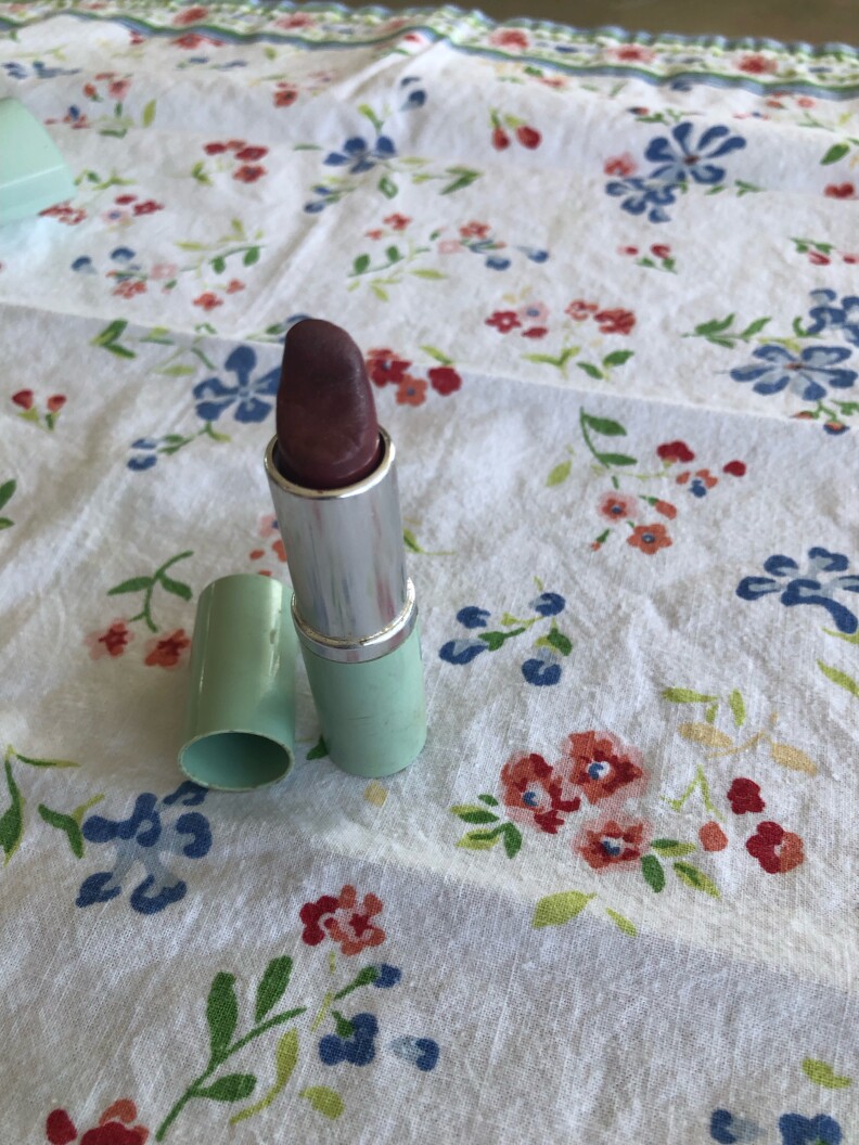 An open tube of dark red lipstick on a floral tablecloth.