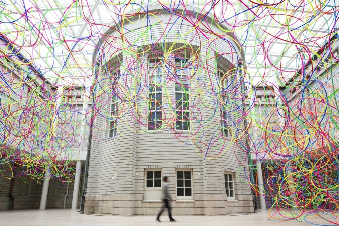 Thousands of multi-colored hula hoops are interconnected and suspended in front of a structure as part of a new art exhibit.
