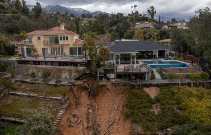Two multi-story homes on the side of a hill bear damage from a mudslide behind their backyards.