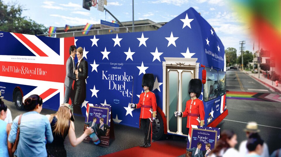 A double decker bus wrapped by stars and the Union Jack with two palace guards stand at attention. 