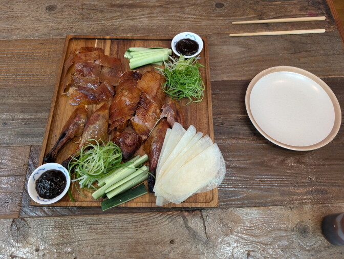 A plate of duck served with Chinese sweet sauce, chopped spring onions and cucumber slices.
