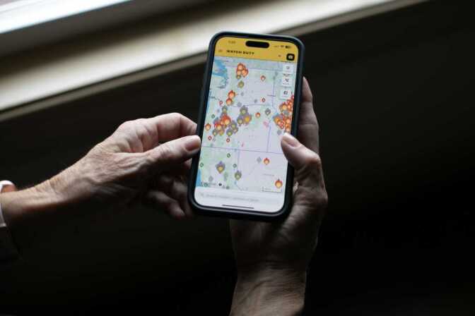 A person's hands hold a phone with flame icons showing the location of fires.