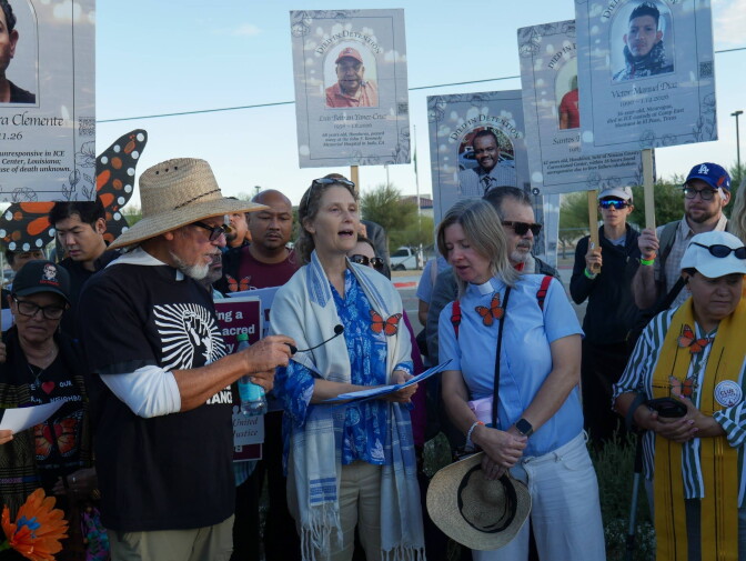 About a dozen people—including interfaith leaders in vestments—stand together along street. They carry signs with faces of different people under the label "died in detention." Some of them have faux monarch butterflies pinned to their clothes. 