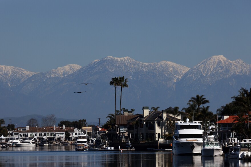Smow capped mountain rise above homes and boats in a marina