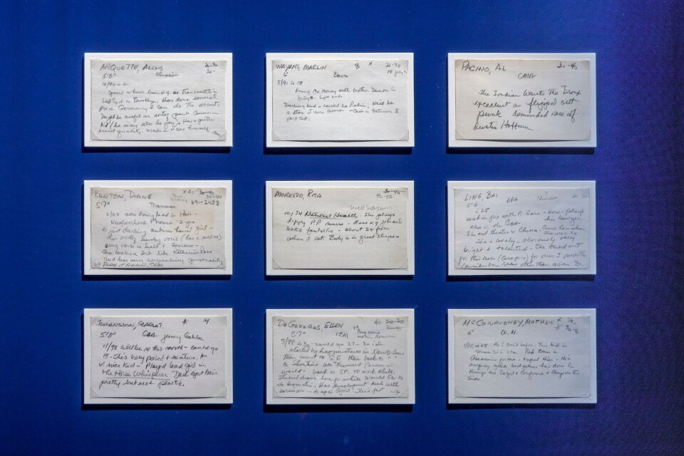 Nine white index cards are displayed in a museum display case — 3 across and 3 down. They each have hand-written notes on them, written in cursive, in pencil or pen, by casting director Marion Dougherty. The top line of each includes the actor’s name (last name, then first name), height, and sometimes age range that they could play. They include notes for Scarlett Johansson, Ellen DeGeneres, Matthew McConaughey, Diane Keaton, Rita Moreno, Bai Ling, Al Pacino, Marlon Wayans, and Alexis Arquette.
