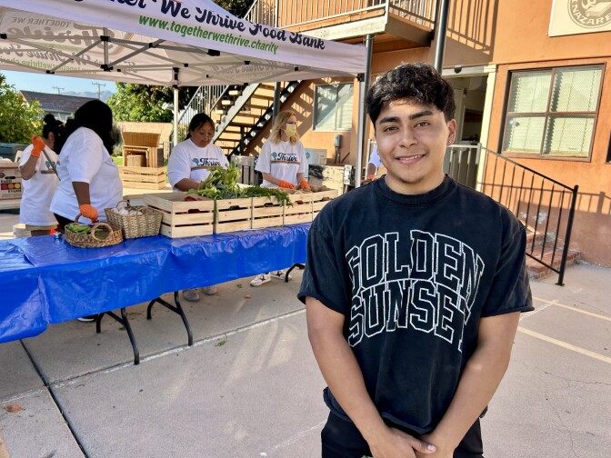 A male presenting person stands in front of folding tables with wood crates on top.