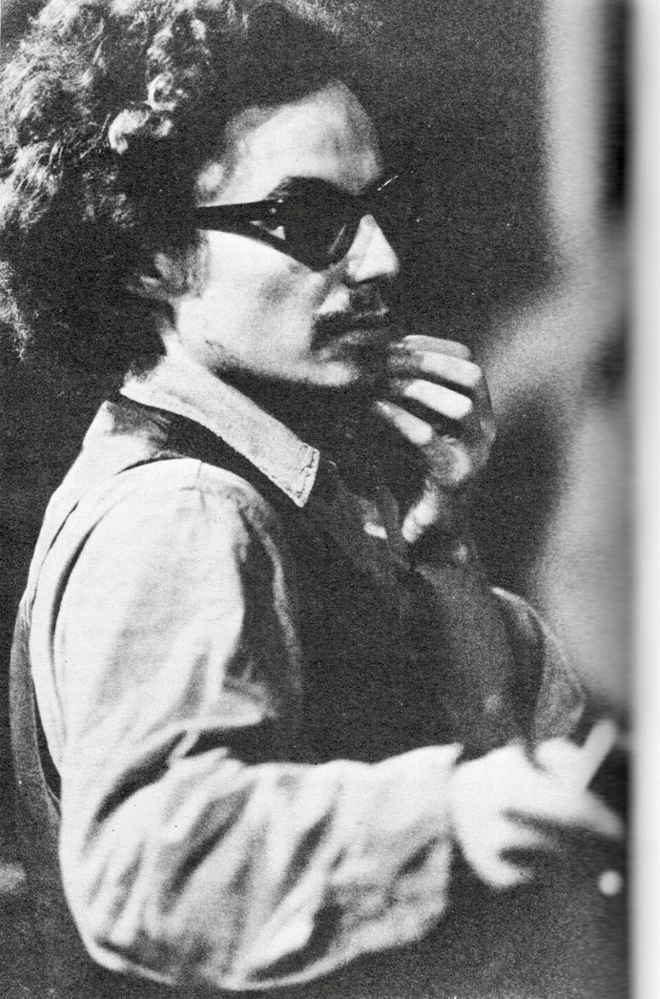 Male presenting person with frizzy hair, wearing dark sunglasses.