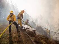 Firefighters work to save burning houses along Linda Flora Drive during the Skirball Fire in Los Angeles, California, December 6, 2017.
The "Skirball" fire ignited before 5 a.m. (1300 GMT) and quickly engulfed some 50 acres, with forecasters predicting the 25-mile-per-hour winds could cause further spreading, threatening multi-million dollar homes and the acclaimed Getty Center museum. / AFP PHOTO / Kyle Grillot        (Photo credit should read KYLE GRILLOT/AFP/Getty Images)