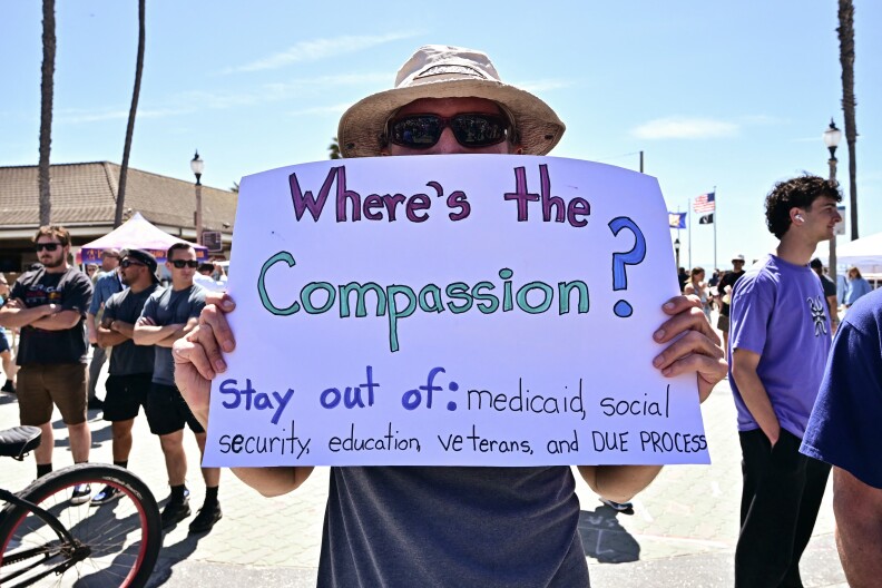 A person holds a handmade sign reading: Where's the compassion? Stay out of: medicaid, social security, education, veterans and due process.