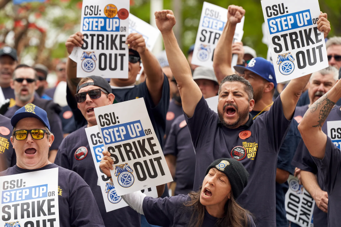 A large group of people, many wearing t-shirts and baseball caps, at a protest. Some are shouting with their arms raised above their heads, others hold signs reading CSU: STEP UP OR STRIKE OUT