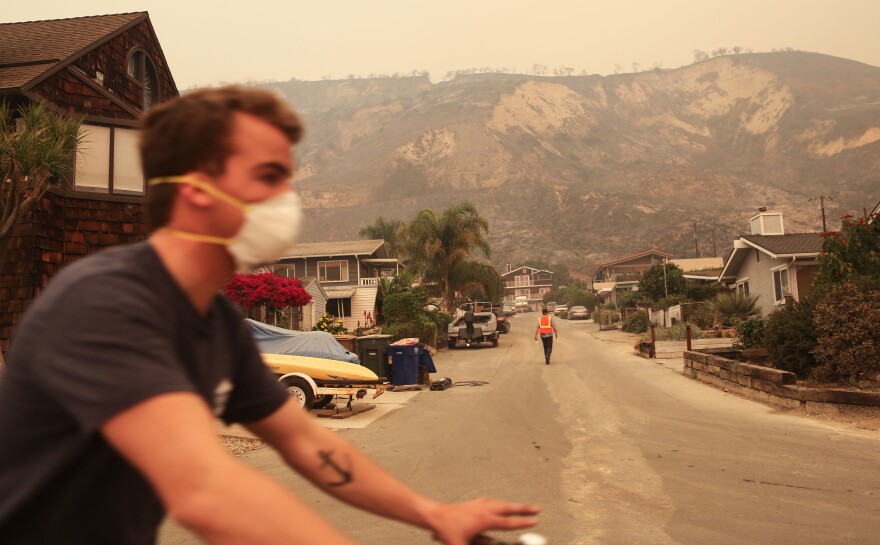 LA CONCHITA, CA - DECEMBER 07:  A man bicycles past bluffs burned in the Thomas Fire on December 7, 2017 in La Conchita, California.  The fire has destroyed 439 structures and burned 115,000 acres.  (Photo by Mario Tama/Getty Images)