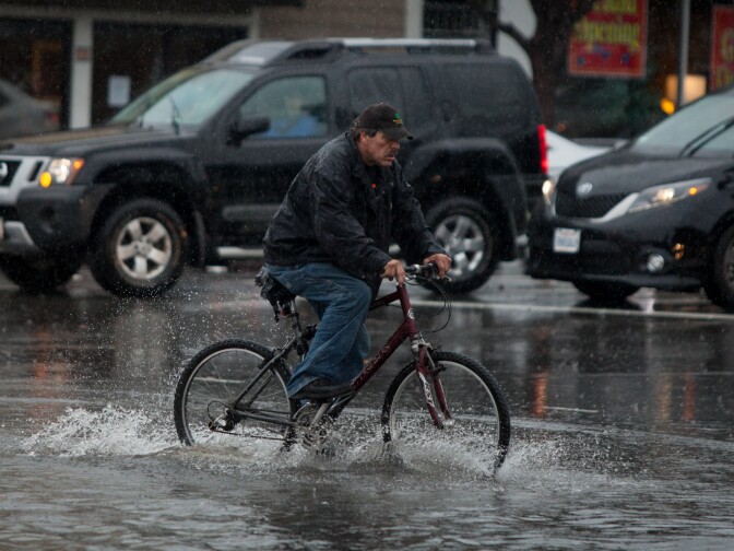 A man rides his bicycle through the flooded intersection of Airport Blvd. and Grand Ave. in South San Francisco, on Thursday, Dec. 11, 2014.  A powerful storm churned through the San Francisco Bay Area on Thursday, knocking out power to tens of thousands and delaying commuters while bringing a soaking of much needed rain.  (AP Photo/Alex Washburn)