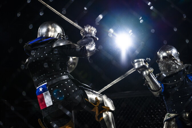 Two armored fighters in helmets clash with swords, one bearing a Texas flag patch, backlit by bright light.