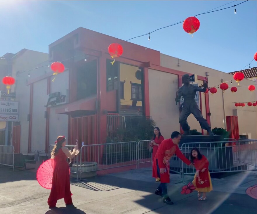 A family of four takes photos in front of the Bruce Lee statue in Chinatown. A man tries to get the little girl to pose.