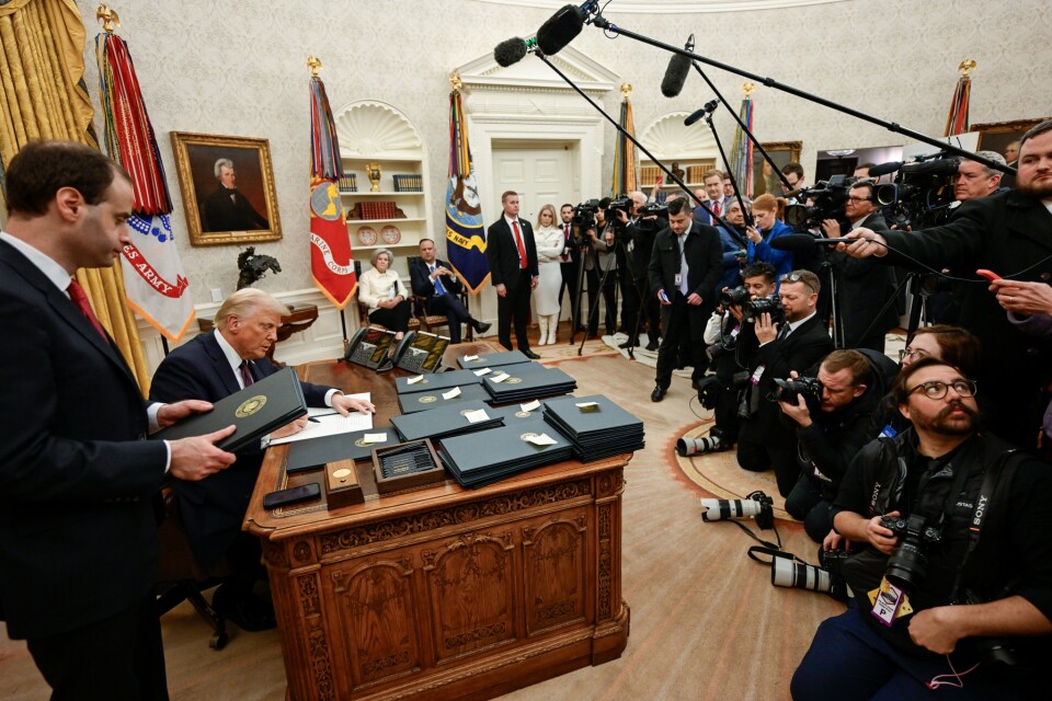 President Donald Trump sits at a desk covered in binders as a room full of reporters looks on.