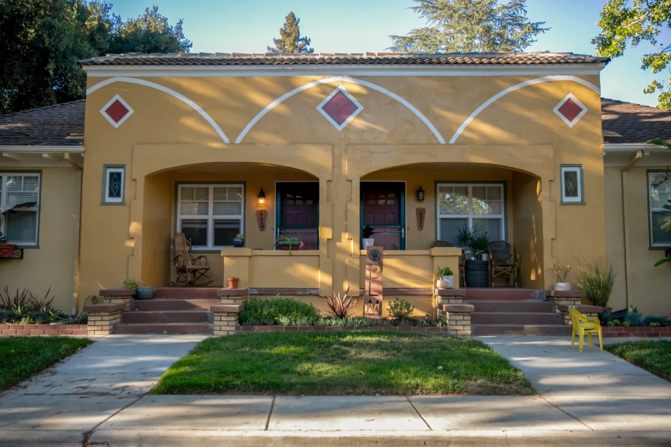 A duplex housing unit is shown, both have front porches and tan paint. 