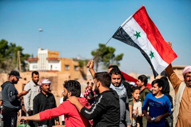 Locals welcome Syrian regime forces as they arrive at the western entrance of the town of Tal Tamr in the countryside of Syria's northeastern Hasakeh province on October 14, 2019. - Syrian regime forces moved towards the Turkish border Monday after Damascus reached a deal with beleaguered Kurdish forces following a US withdrawal announcement, AFP correspondents reported. Soldiers waving Syrian flags deployed west of Tall Tamr, not far from the flashpoint border town of Ras al-Ain, which has been a key target of Turkish forces and their proxies since they launched their onslaught six days ago. (Photo by Delil SOULEIMAN / AFP) (Photo by DELIL SOULEIMAN/AFP via Getty Images)