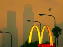 A McDonald's fast-food restaurant sign glows above the city skyline located in the Figueroa Corridor area of South Los Angeles, Los Angeles, California.