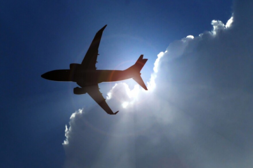 An image of a commercial airplane silhouetted against white clouds and a blue sky.