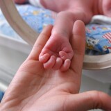 A parent holds the hand of their newborn child