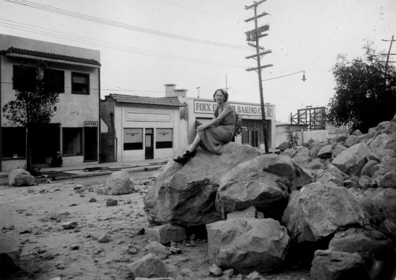 From Nov. 9, 1937: "Elysian Park Landslide on Riverside Drive, looking east from Arnold Street, showing large boulders in roadway, girl sitting on top of boulder. Foix French Baking Co."

