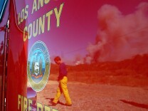 A firefighter and smoke from a huge wildfire are reflected in a Los Angeles County Fire Department fire engine near highway 118 in this file photo taken October 27, 2003 in Simi Valley, California. The county fire department has been under scrutiny recently over evidence of cheating on its admissions exams.