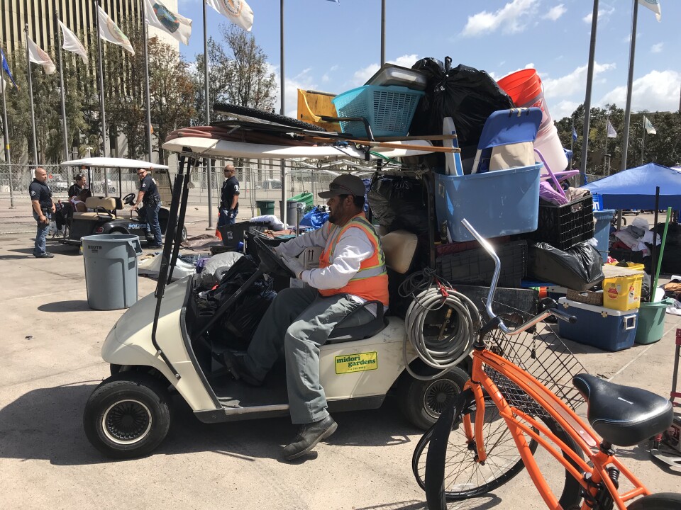 A worker carts trash from the Civic Center homeless encampment to a dumpster. April 12, 2018. 