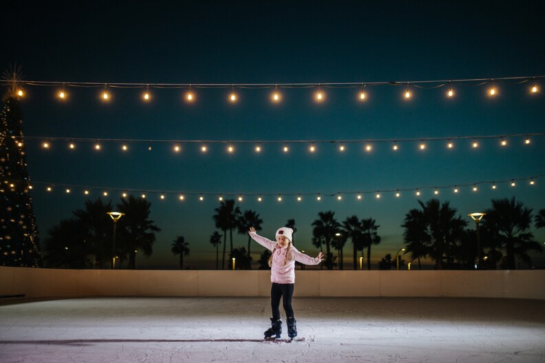 a young girl in a pink jacket skates alone on an ice rink at night