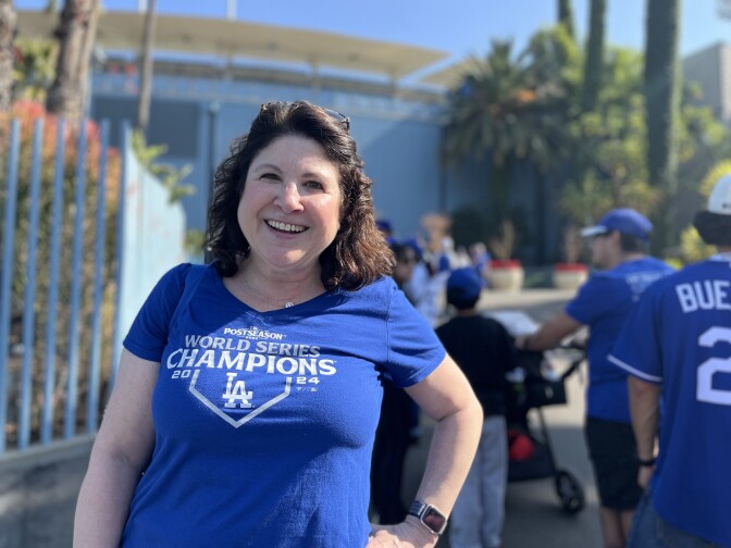 A woman with brown hair wearing a blue "World Series Champions" Dodgers shirt poses outside Dodger Stadium.