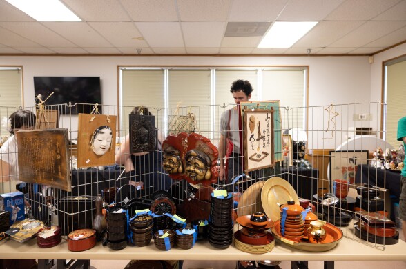 A table lined with lacquer bowls and boxes, with Japanese sculptural artwork hanging from a display.