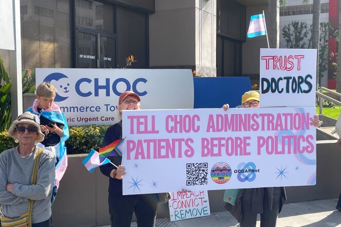 Protesters holding trans and LGBTQ+ pride flags pose for a photo outside Children Hospital of Orange County. Their signs say "Tell CHOC administration: Patients before politics," "Impeach, convict, and remove," and "Trust doctors."