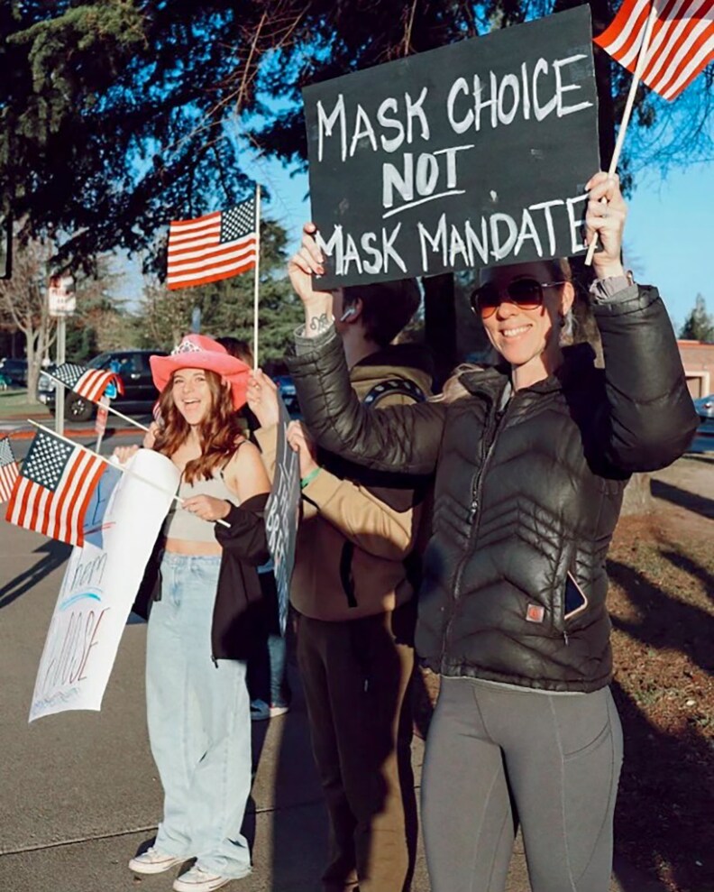 A group of people hold up signs and American flags while standing outside. The sign reads: "Mask Choice Not Mask Mandate."