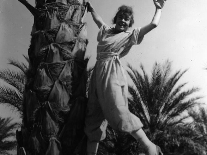 An undated photo of a woman frolicking with a date palm, probably in the Coachella Valley.