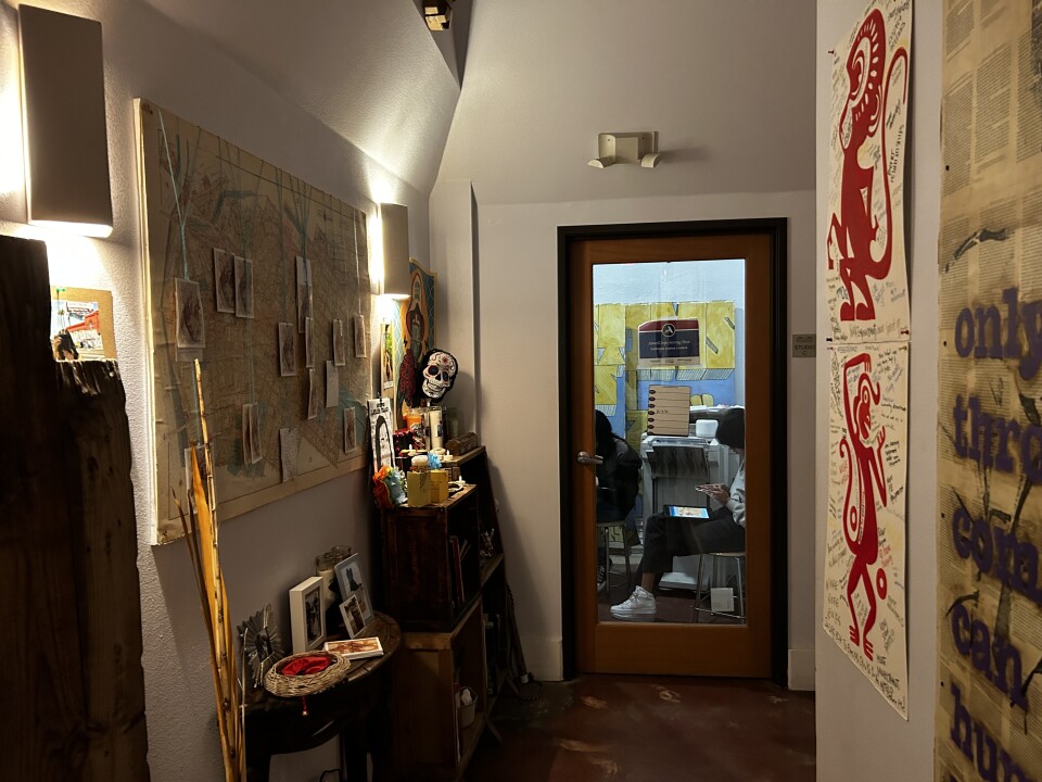 A hallway lined with posters and artwork that ends in a clear door with a room where students work on ipads. 