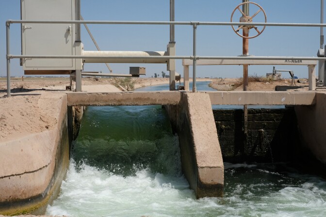 Water gushes from a cement irrigation gate on a sunny day. 