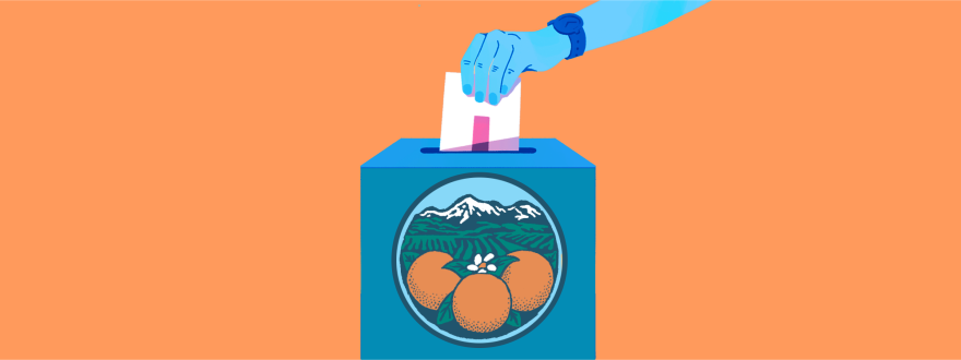 A person's hand drops a ballot into a ballot box with oranges and a view to snow-capped mountains