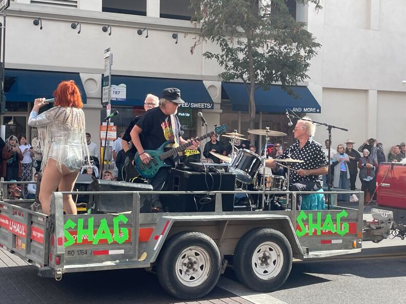 A band of four people on a trailer with the word "Shag" taped on in the side. It's a standard rock combo: a vocalist, a bass player, a guitarist, and a drummer.