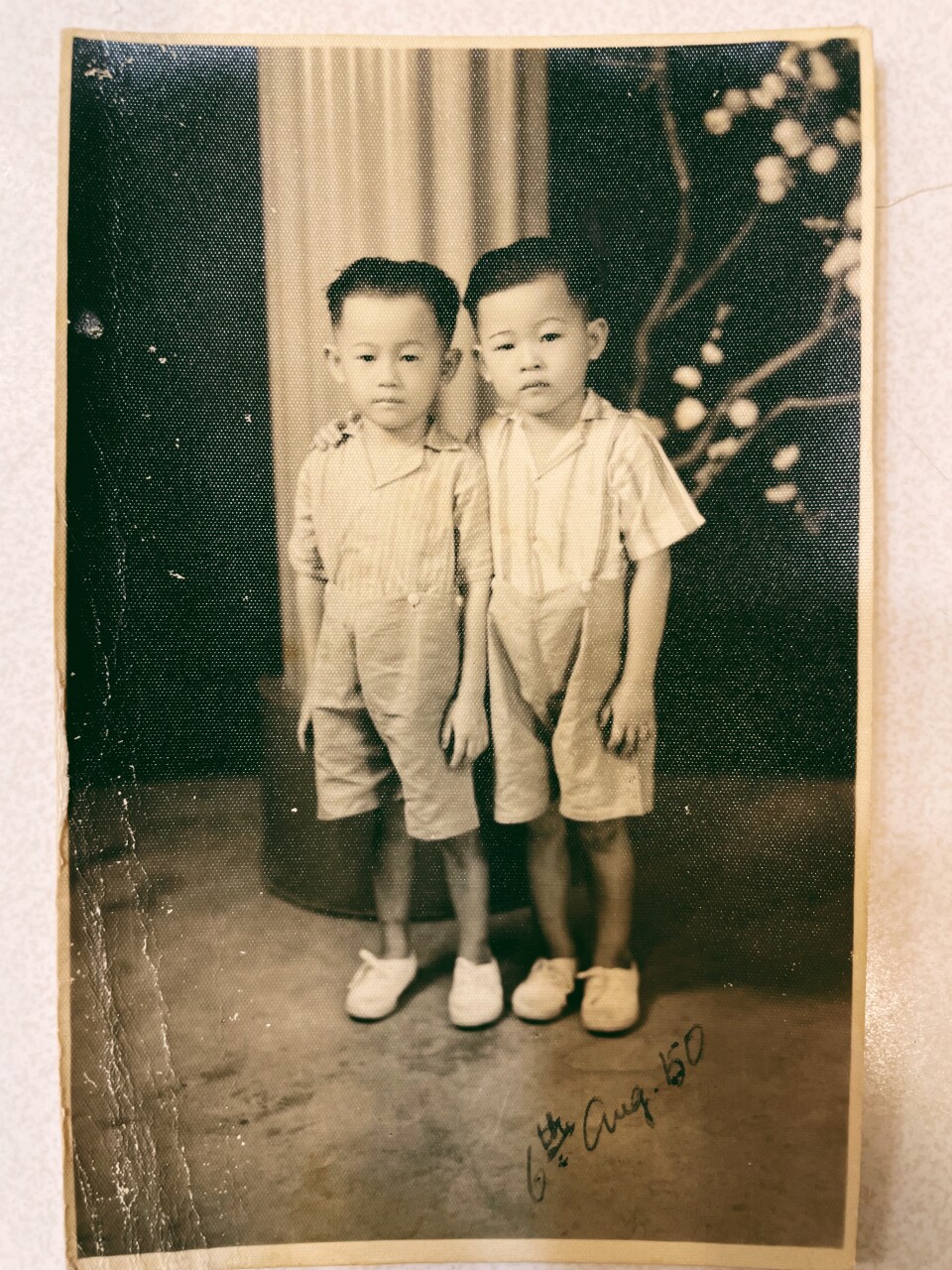 A black and white photo of twin boys in linen-shorts and suspenders and white sneakers.