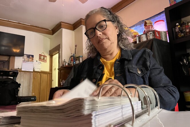 Cristina Campos sits at her family's kitchen table and flips through a binder of paperwork related to her apartment of 23 years.