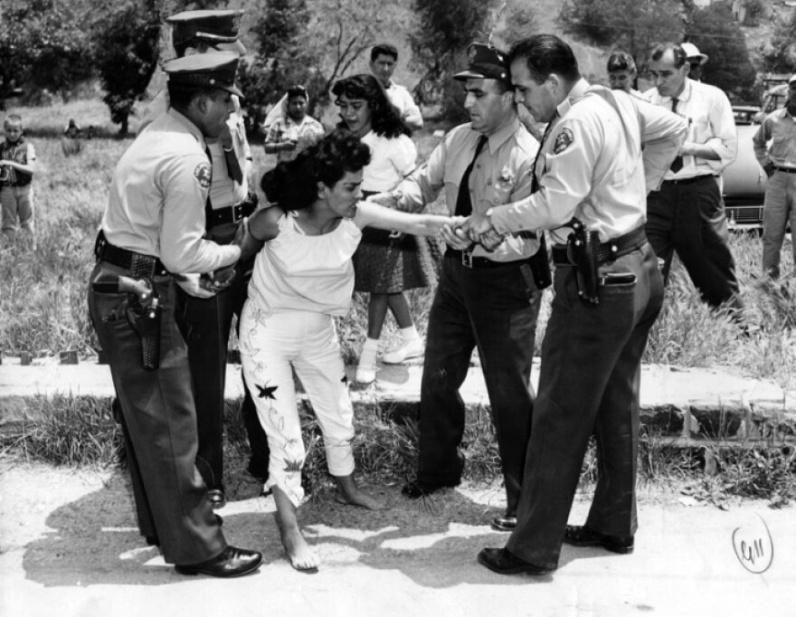 L.A. County Sheriff deputies in uniform forcibly remove woman from her home, tugging on her arms as she struggles.