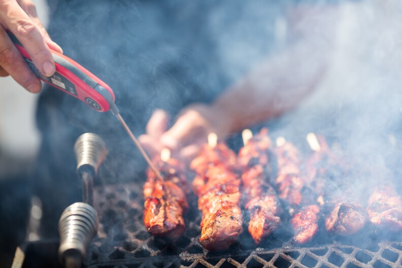 Un hombre usa un termómetro para carne para comprobar un kebab a la parrilla.