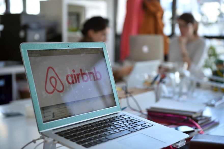 A laptop sits in an office setting. The airbnb logo is on the screen.