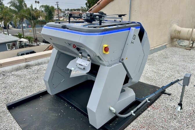 A small drone on a landing pad on a rooftop with palm trees in the background.